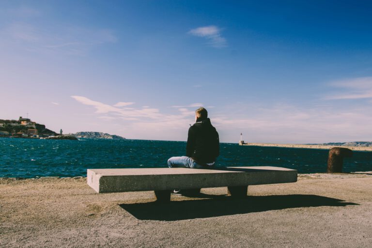 "Imagen de un chico reflexionando en un banco con vista al mar y la montaña"