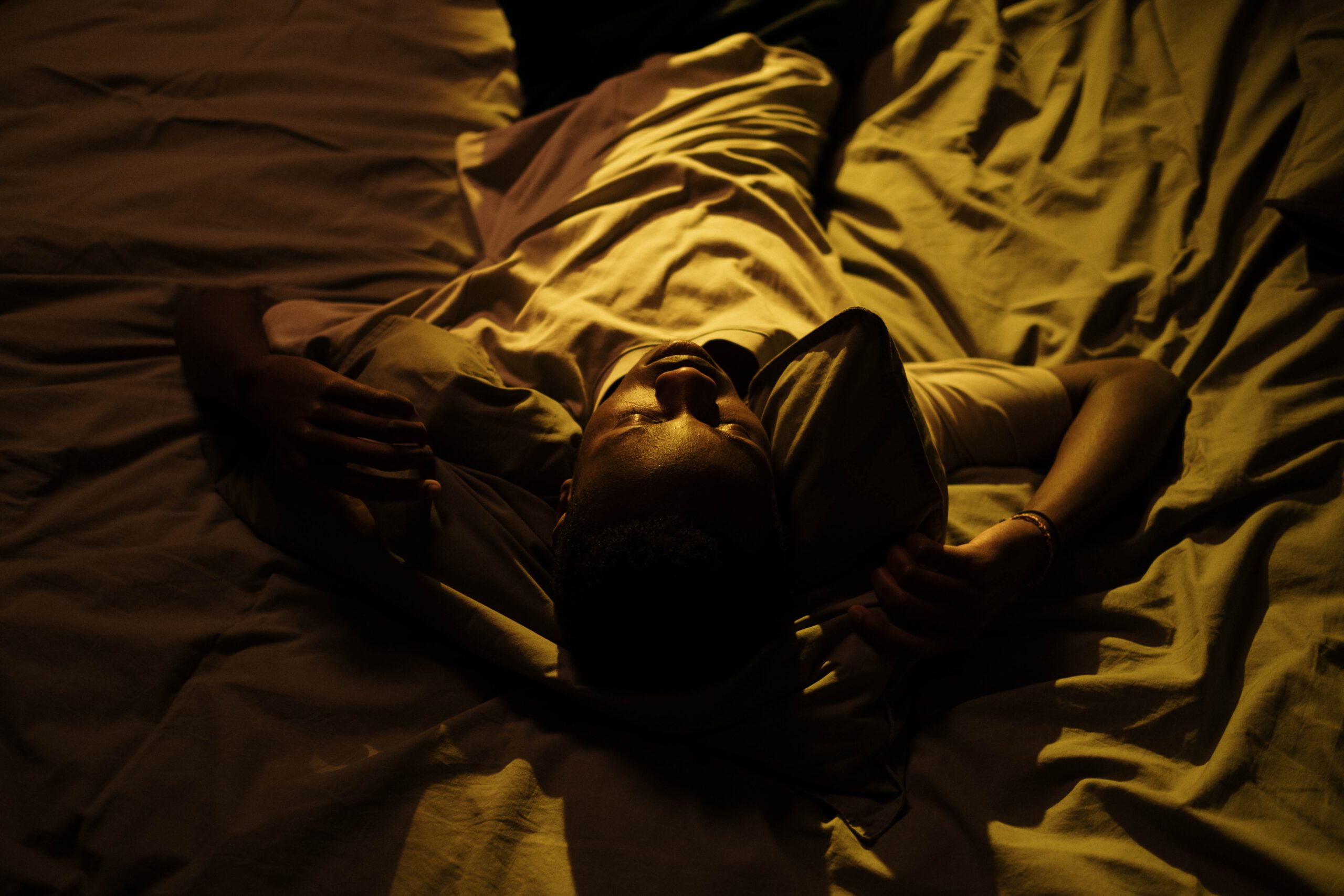 "Ansiedad y preocupación: Chico negro tumbado en una cama blanca durante la noche"