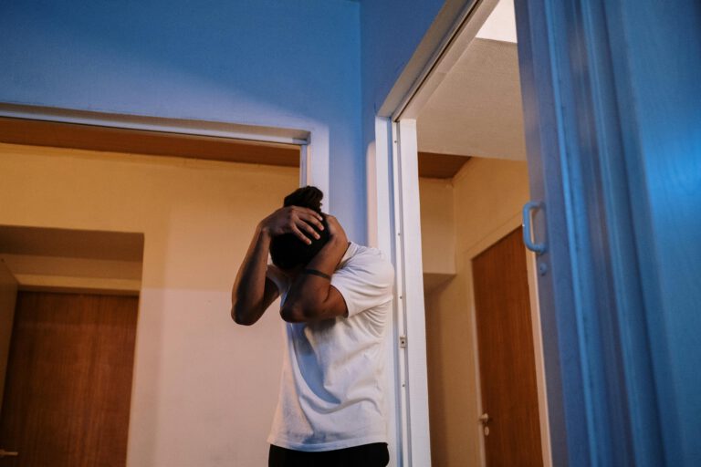 Persona con camiseta blanca, cabizbaja y con las manos sobre la cabeza en señal de sufrimiento, representando la disociación dentro de una habitación.