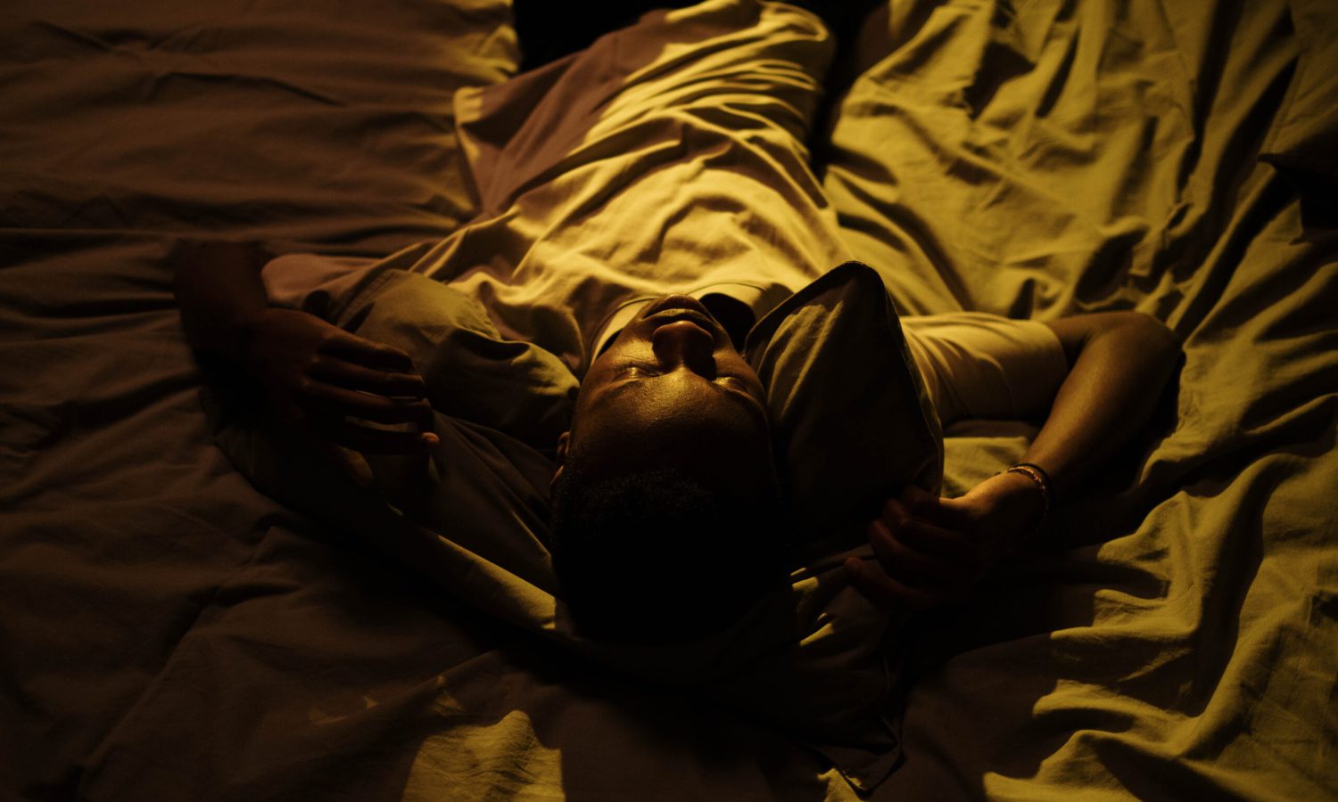 "Ansiedad y preocupación: Chico negro tumbado en una cama blanca durante la noche"
