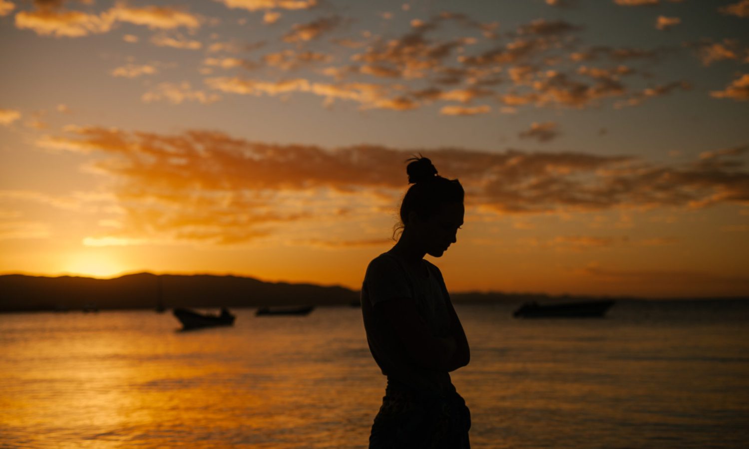 Silueta de una chica practicando mindfulness en un atardecer anaranjado junto al mar
